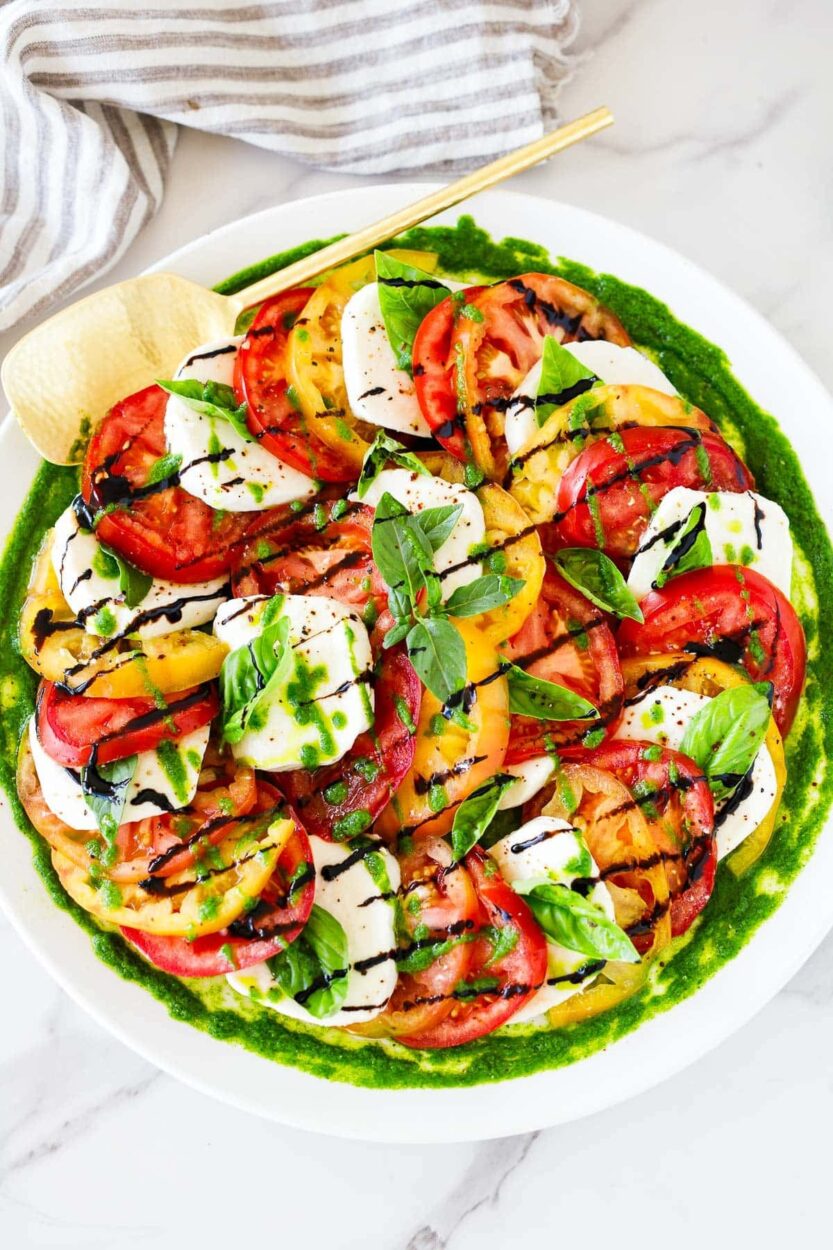 Caprese Salad beautifully plated on a white marble board with sliced ripe tomatoes, fresh mozzarella, basil leaves, and a drizzle of balsamic glaze and olive oil