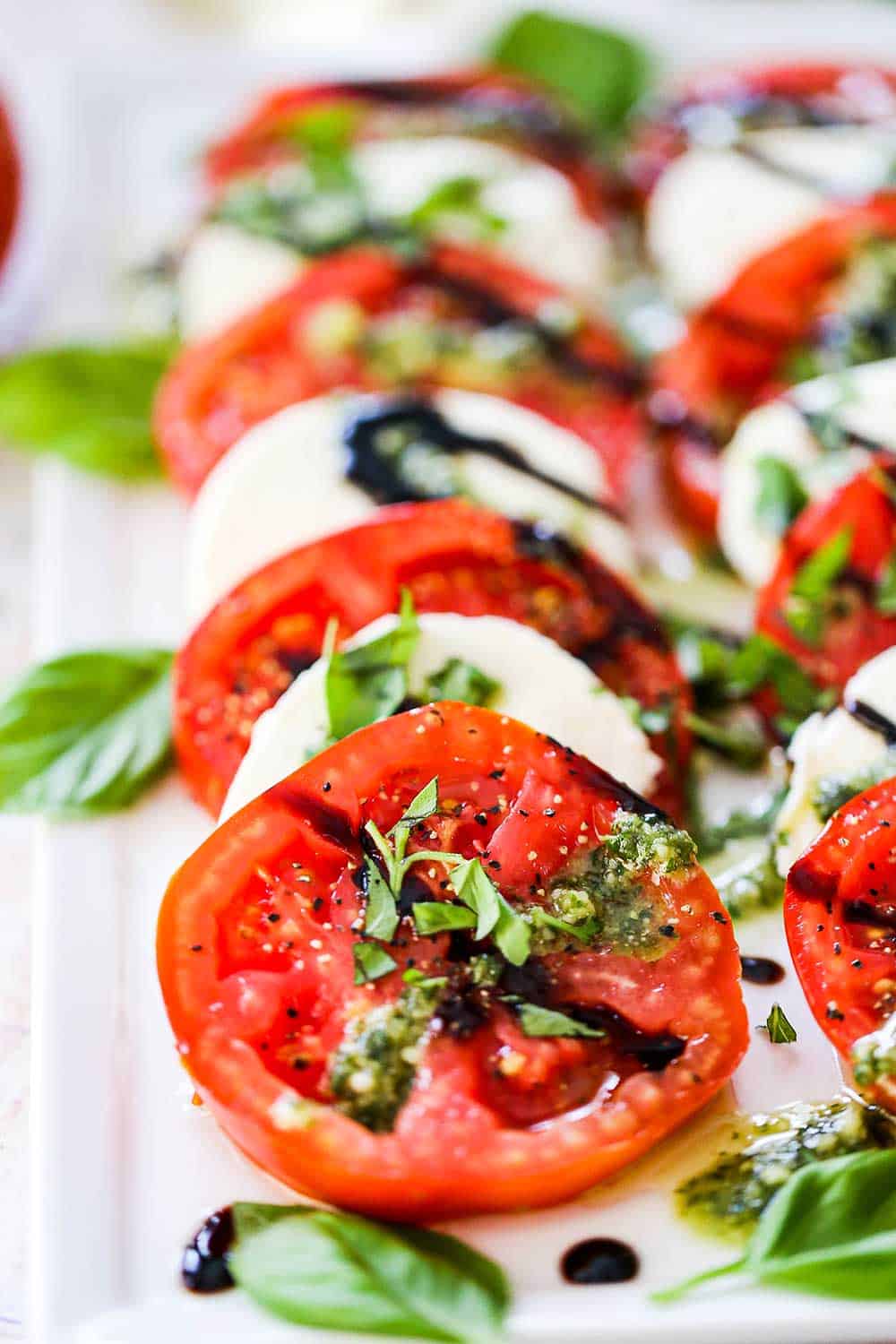 Close-up of a Caprese Salad serving on a white plate showing the glossy balsamic glaze drizzle over layered tomato and mozzarella slices with fresh basil leaves and a crack of black pepper