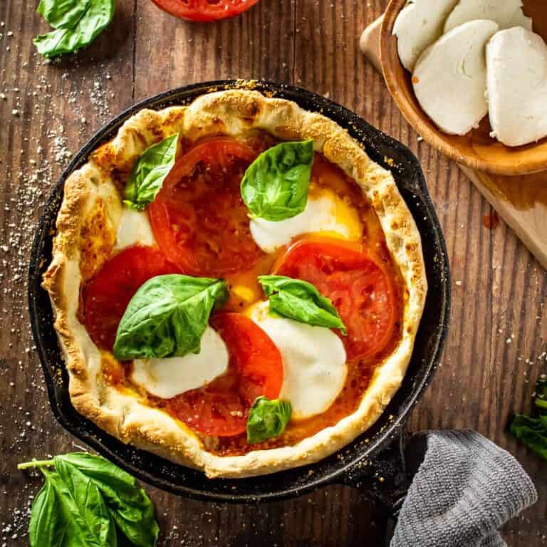Close-up of a perfectly sliced cast iron skillet pizza with golden crispy bottom crust visible, stretchy mozzarella cheese pull, and bubbling tomato sauce with fresh basil and red pepper flakes on top