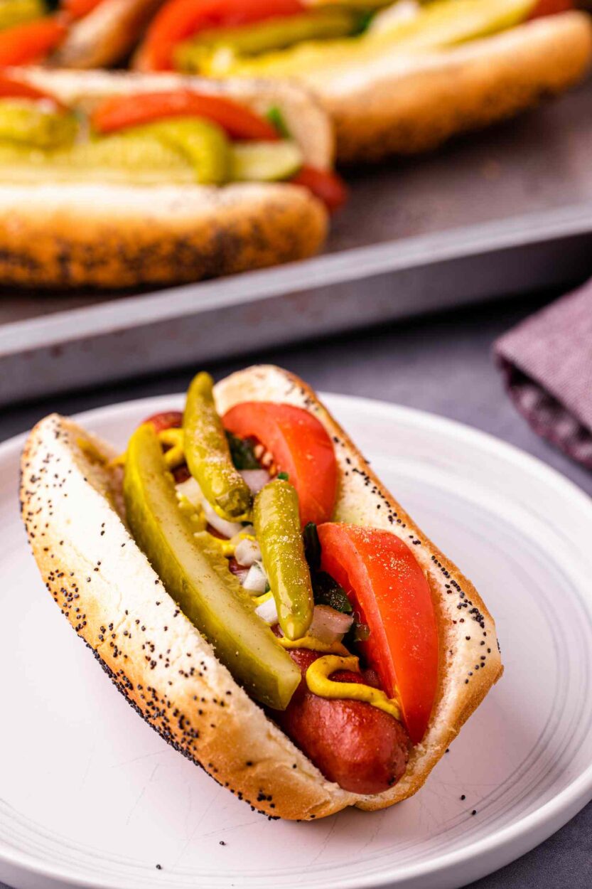 Close-up of a finished Chicago Style Hot Dog in a poppy seed bun, showing the neon green relish, yellow mustard, sport peppers, and a glistening dill pickle spear in sharp detail against a rustic background