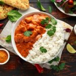 Chicken Tikka Masala served in a white bowl with naan bread, garnished with fresh cilantro and a swirl of cream, overhead shot on a dark wooden table
