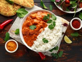 Chicken Tikka Masala served in a white bowl with naan bread, garnished with fresh cilantro and a swirl of cream, overhead shot on a dark wooden table
