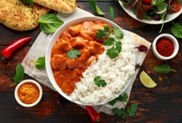 Chicken Tikka Masala served in a white bowl with naan bread, garnished with fresh cilantro and a swirl of cream, overhead shot on a dark wooden table