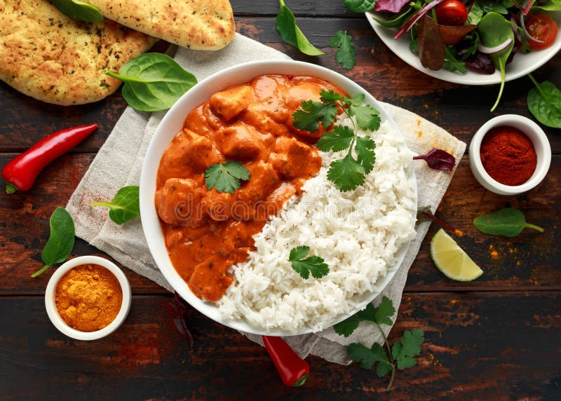 Chicken Tikka Masala served in a white bowl with naan bread, garnished with fresh cilantro and a swirl of cream, overhead shot on a dark wooden table