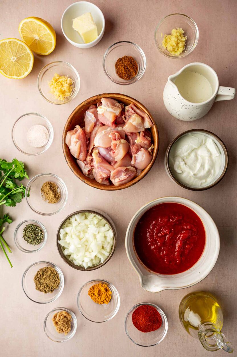 Ingredients for Chicken Tikka Masala laid out flat on a marble surface including whole spices, yogurt, crushed tomatoes, fresh ginger, garlic, and raw chicken thighs