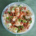 Classic Potato Salad served in a large white bowl, garnished with paprika and fresh chives, surrounded by a wooden picnic table setting