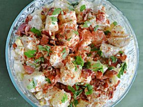 Classic Potato Salad served in a large white bowl, garnished with paprika and fresh chives, surrounded by a wooden picnic table setting