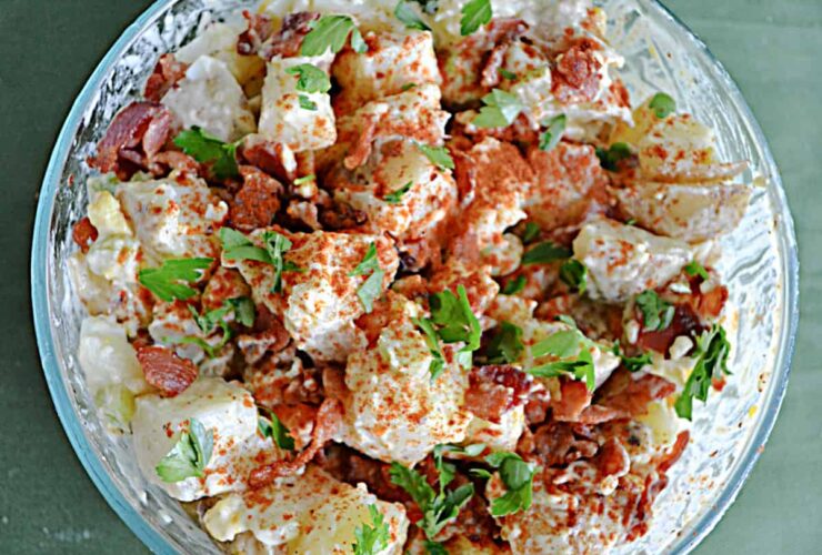 Classic Potato Salad served in a large white bowl, garnished with paprika and fresh chives, surrounded by a wooden picnic table setting