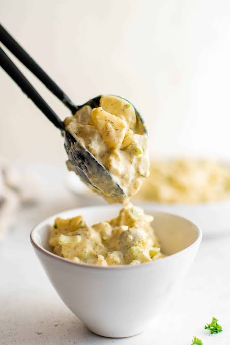 Close-up of Classic Potato Salad being scooped with a large spoon, showing creamy dressing, chunks of potato, egg, and celery with a dusting of paprika