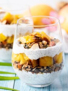 Coconut chia pudding parfait breakfast served in tall glass jars layered with mango, toasted granola, and toasted coconut flakes on a bright tropical table setting
