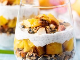 Coconut chia pudding parfait breakfast served in tall glass jars layered with mango, toasted granola, and toasted coconut flakes on a bright tropical table setting
