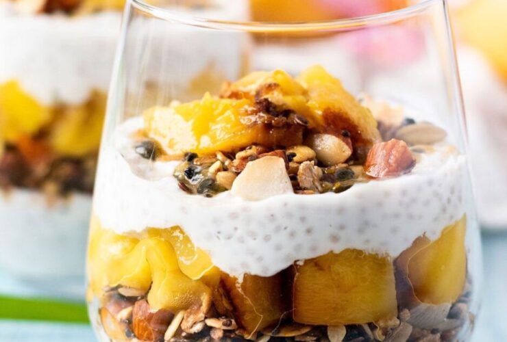 Coconut chia pudding parfait breakfast served in tall glass jars layered with mango, toasted granola, and toasted coconut flakes on a bright tropical table setting