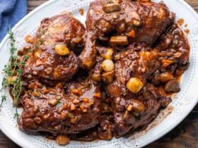Coq au Vin served in a rustic Dutch oven with glossy red wine sauce, mushrooms, pearl onions, and fresh thyme garnish on a wooden table