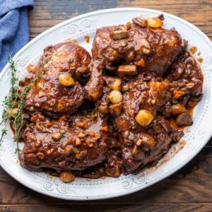 Coq au Vin served in a rustic Dutch oven with glossy red wine sauce, mushrooms, pearl onions, and fresh thyme garnish on a wooden table