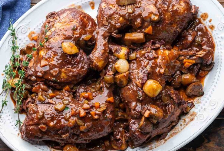 Coq au Vin served in a rustic Dutch oven with glossy red wine sauce, mushrooms, pearl onions, and fresh thyme garnish on a wooden table
