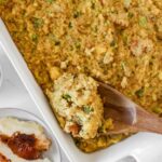 Golden Southern cornbread dressing fresh from the oven in a large baking dish, crispy top with herbs visible, rustic Thanksgiving table setting