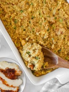 Golden Southern cornbread dressing fresh from the oven in a large baking dish, crispy top with herbs visible, rustic Thanksgiving table setting