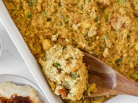 Golden Southern cornbread dressing fresh from the oven in a large baking dish, crispy top with herbs visible, rustic Thanksgiving table setting