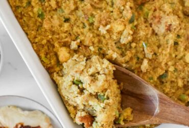 Golden Southern cornbread dressing fresh from the oven in a large baking dish, crispy top with herbs visible, rustic Thanksgiving table setting