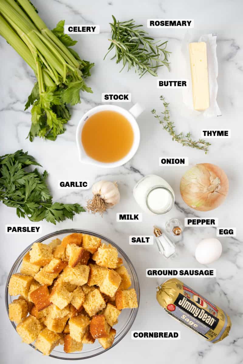 Step-by-step ingredients flat lay for cornbread dressing — crumbled cornbread in a large bowl, eggs, celery, onion, fresh sage, and broth measured out on a wooden kitchen counter