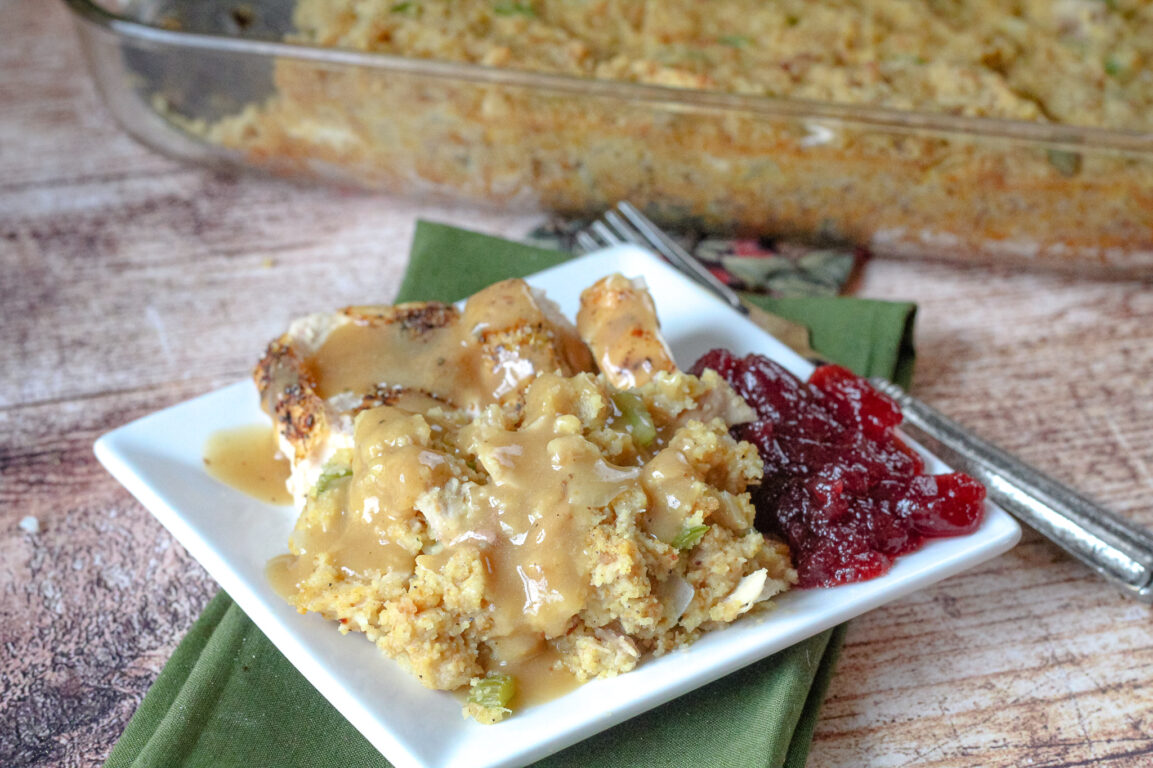 Close-up of a serving spoon lifting a scoop of Southern cornbread dressing onto a plate, showing the golden crust and tender herby interior, with gravy poured over the top