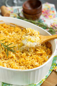 Golden creamed corn casserole in a white baking dish, fresh from the oven with a slightly puffed top and caramelized edges, surrounded by a rustic holiday table setting