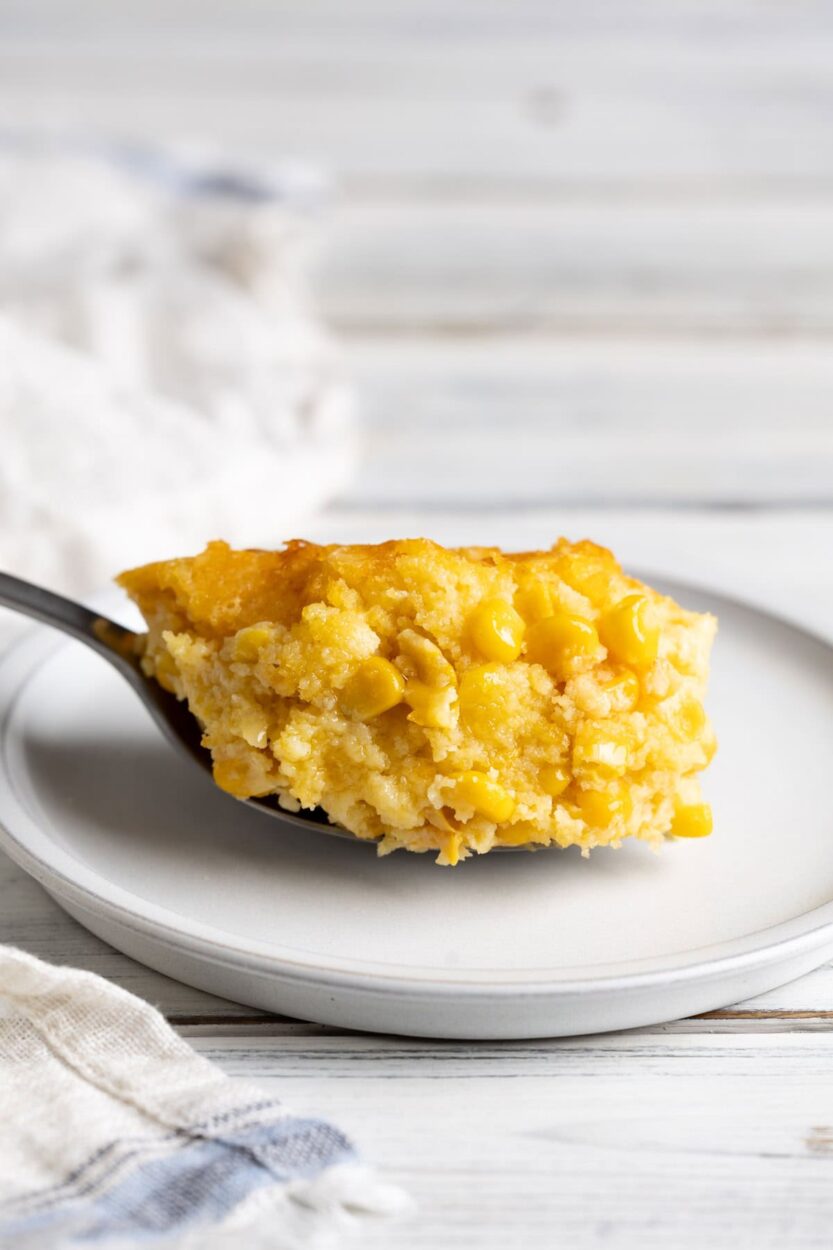 Close-up of a spoonful of creamed corn casserole being lifted from the dish, showing the tender, custardy interior and golden top