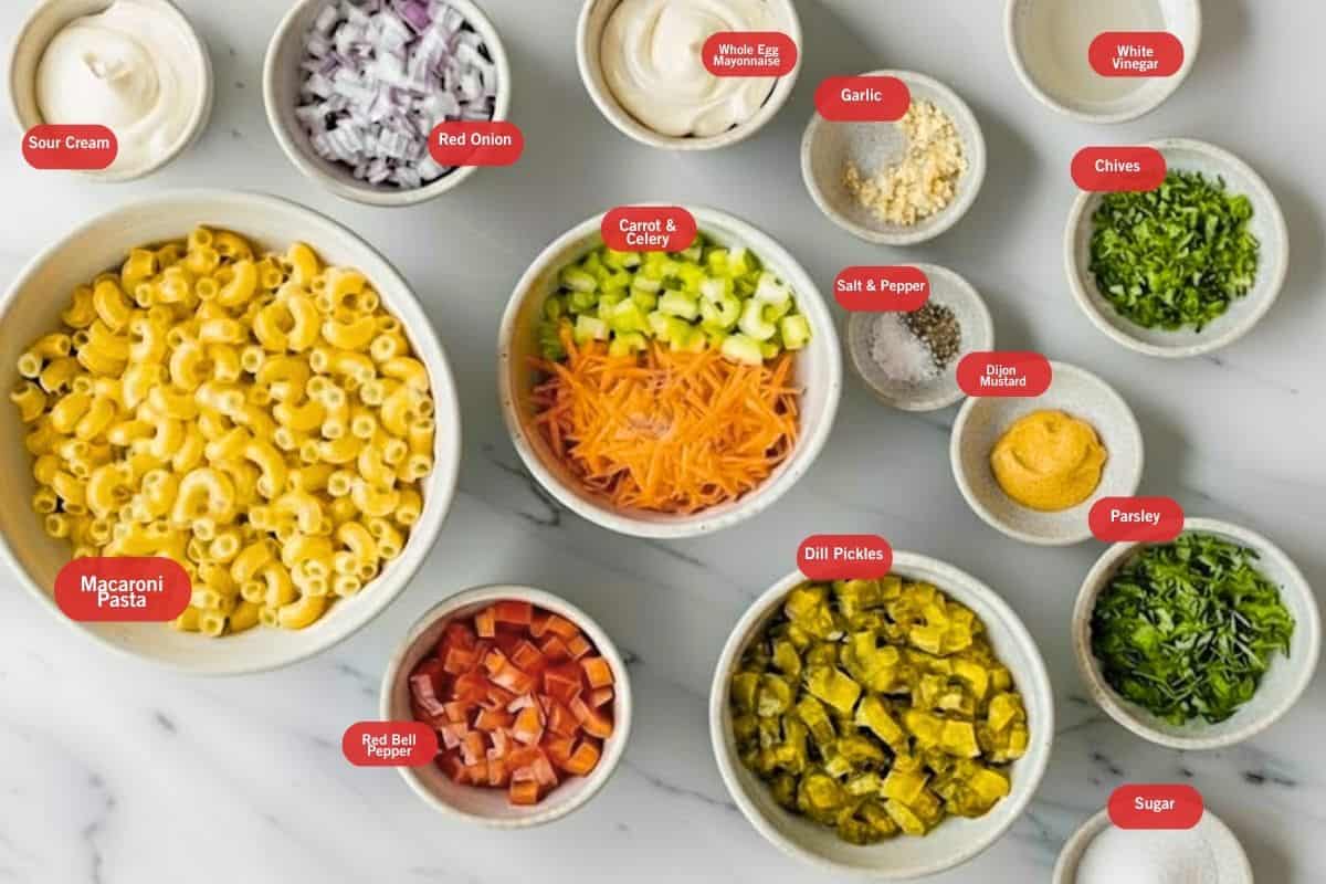 A flat lay of ingredients for creamy macaroni salad including elbow macaroni, mayonnaise, celery, red onion, bell pepper, mustard, and relish arranged on a white marble surface