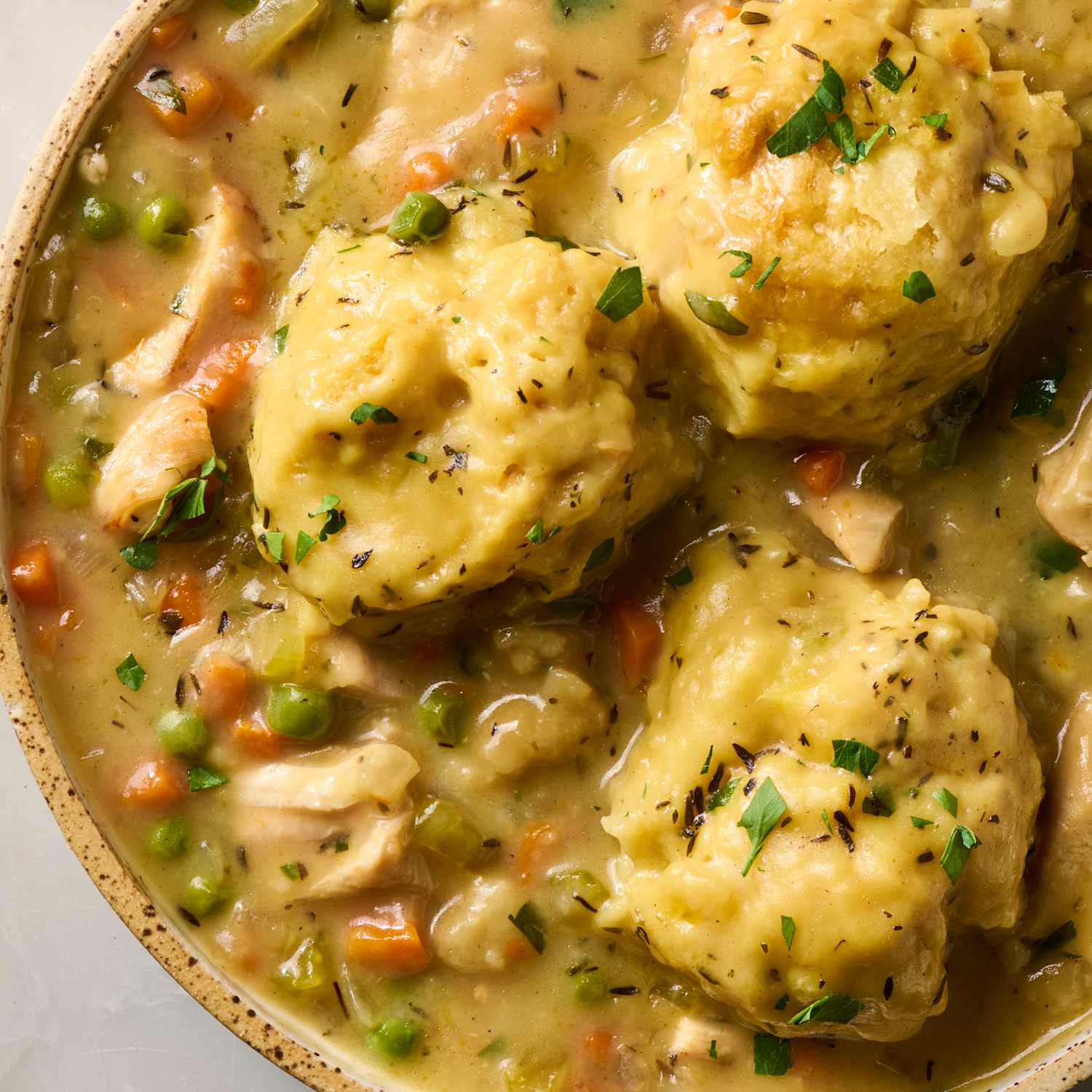 Close-up of Crockpot Chicken and Dumplings in a rustic bowl, showing the creamy broth, shredded chicken, and a fluffy dumpling torn open to reveal its soft interior