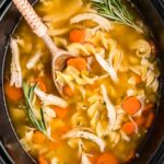 A steaming bowl of Crockpot Chicken Noodle Soup with golden broth, tender chicken, carrots, celery, and egg noodles, garnished with fresh parsley on a rustic wooden table