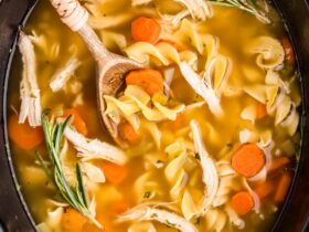 A steaming bowl of Crockpot Chicken Noodle Soup with golden broth, tender chicken, carrots, celery, and egg noodles, garnished with fresh parsley on a rustic wooden table