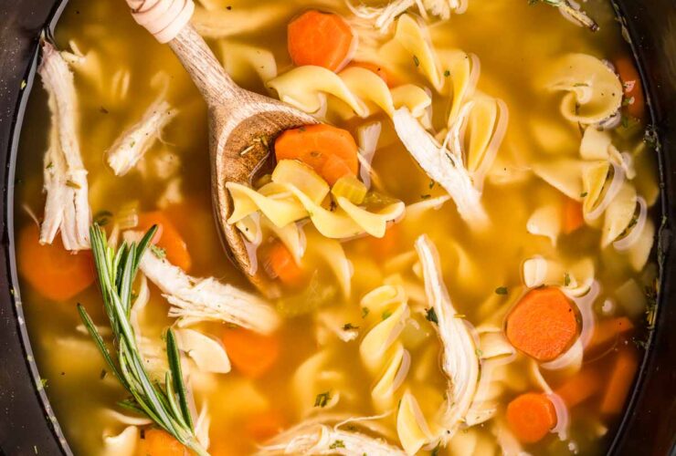 A steaming bowl of Crockpot Chicken Noodle Soup with golden broth, tender chicken, carrots, celery, and egg noodles, garnished with fresh parsley on a rustic wooden table