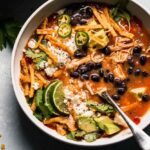 Crockpot Chicken Tortilla Soup served in a wide bowl topped with crispy tortilla strips, shredded cheese, sour cream, avocado slices, and fresh cilantro, photographed overhead on a rustic wooden table