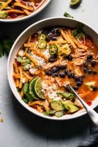 Crockpot Chicken Tortilla Soup served in a wide bowl topped with crispy tortilla strips, shredded cheese, sour cream, avocado slices, and fresh cilantro, photographed overhead on a rustic wooden table