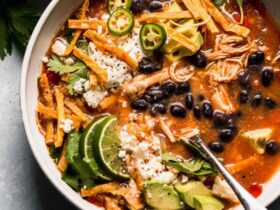 Crockpot Chicken Tortilla Soup served in a wide bowl topped with crispy tortilla strips, shredded cheese, sour cream, avocado slices, and fresh cilantro, photographed overhead on a rustic wooden table