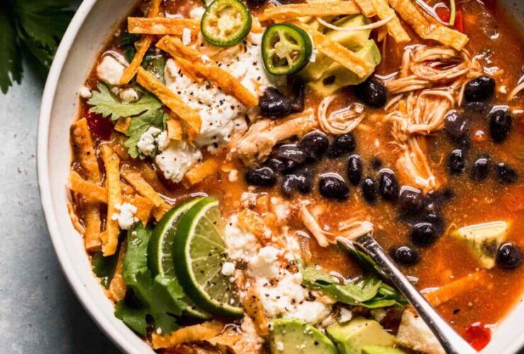 Crockpot Chicken Tortilla Soup served in a wide bowl topped with crispy tortilla strips, shredded cheese, sour cream, avocado slices, and fresh cilantro, photographed overhead on a rustic wooden table