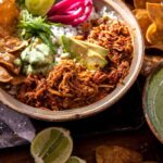 Crockpot Salsa Chicken piled high in a rustic bowl, garnished with fresh cilantro, sliced avocado, and a squeeze of lime, served with warm tortillas on a wooden board