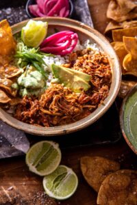 Crockpot Salsa Chicken piled high in a rustic bowl, garnished with fresh cilantro, sliced avocado, and a squeeze of lime, served with warm tortillas on a wooden board