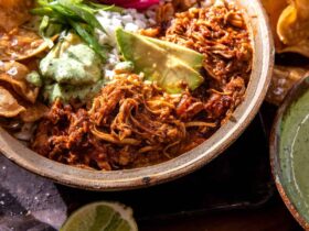 Crockpot Salsa Chicken piled high in a rustic bowl, garnished with fresh cilantro, sliced avocado, and a squeeze of lime, served with warm tortillas on a wooden board