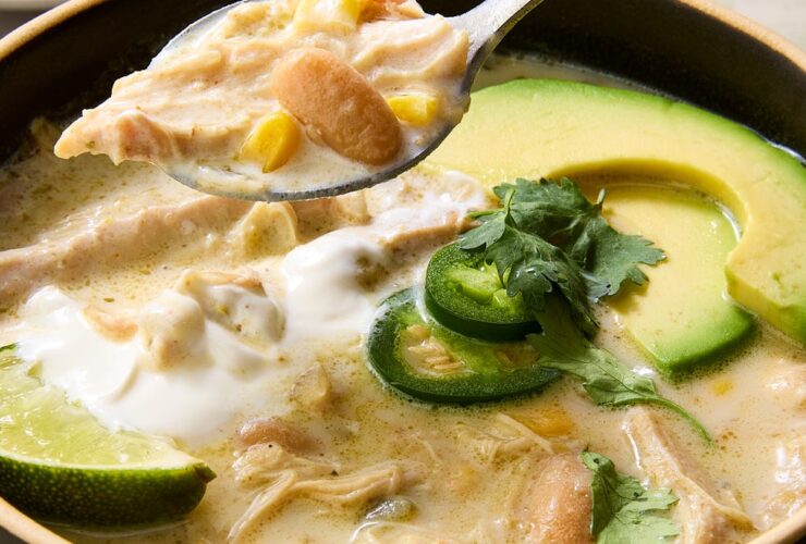 Crockpot white chicken chili served in a rustic bowl topped with sour cream, shredded cheese, jalapeño slices, cilantro, and a squeeze of lime on a dark moody surface