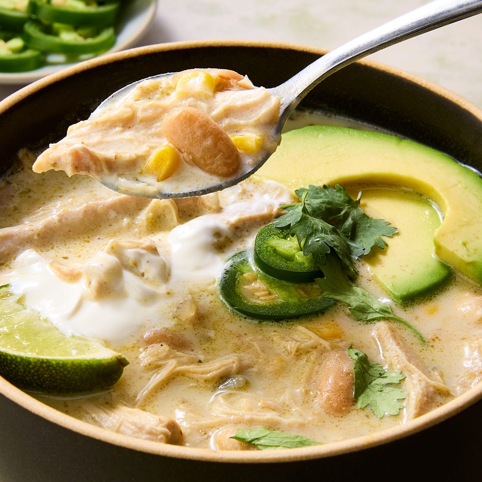 Crockpot white chicken chili served in a rustic bowl topped with sour cream, shredded cheese, jalapeño slices, cilantro, and a squeeze of lime on a dark moody surface
