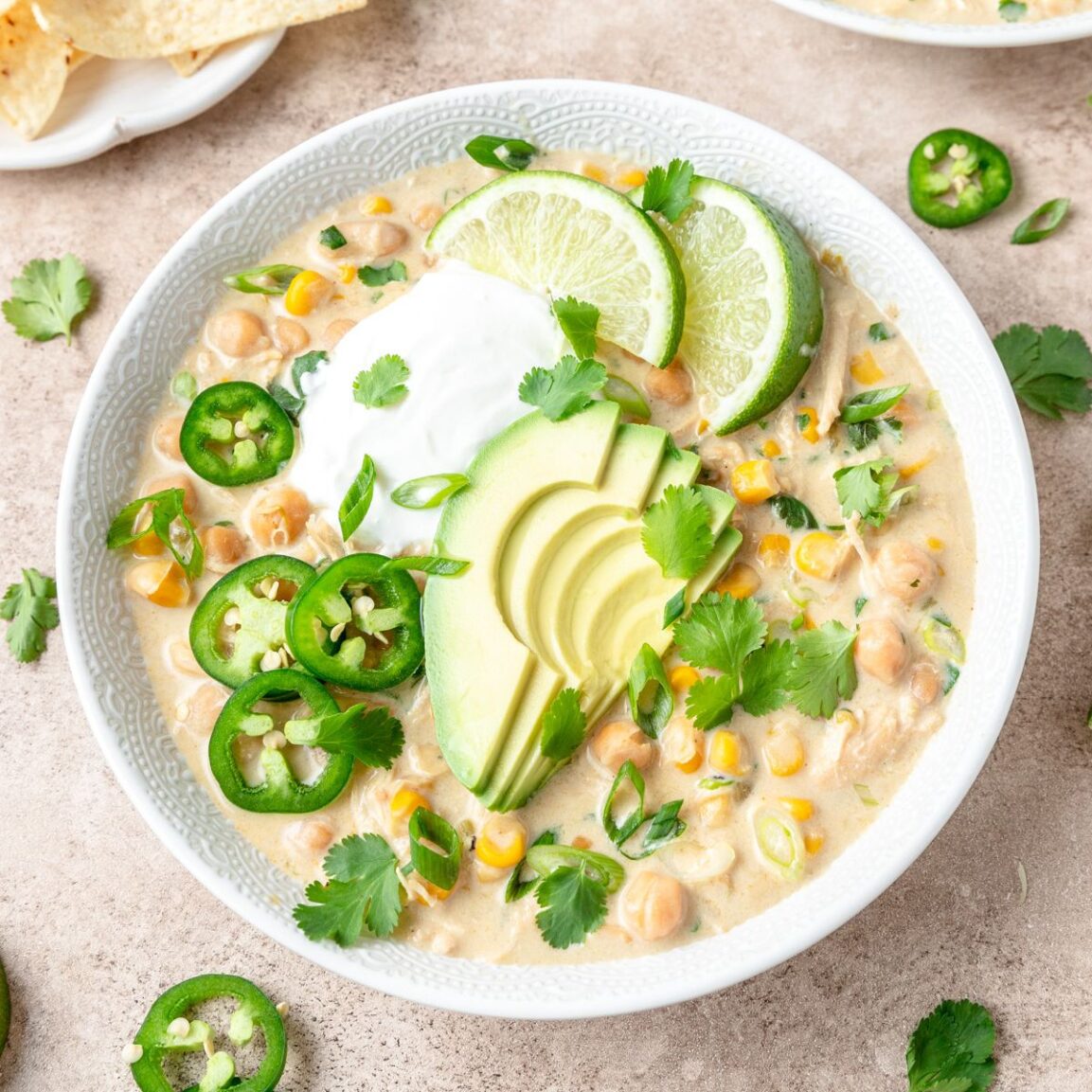 Close-up overhead shot of a bowl of white chicken chili with thick, creamy broth, shredded chicken, white beans, topped with avocado slices, tortilla strips, and fresh cilantro