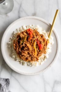 Cuban Ropa Vieja served over white rice in a rustic bowl, garnished with green olives and fresh cilantro, rich red tomato sauce glistening under warm light
