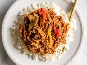 Cuban Ropa Vieja served over white rice in a rustic bowl, garnished with green olives and fresh cilantro, rich red tomato sauce glistening under warm light