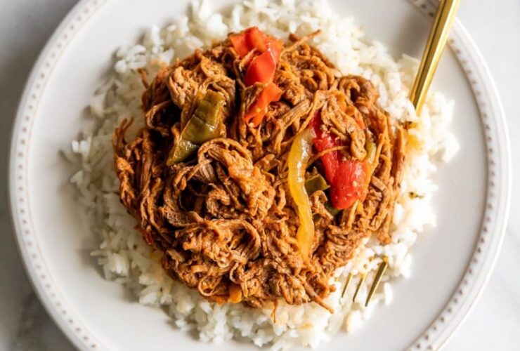 Cuban Ropa Vieja served over white rice in a rustic bowl, garnished with green olives and fresh cilantro, rich red tomato sauce glistening under warm light