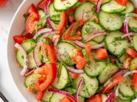 Cucumber tomato salad in a white bowl with red onion, fresh dill, and a glossy vinaigrette dressing — overhead shot on a rustic wooden table