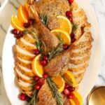Whole dry brined roast turkey on a wooden carving board, golden brown shatteringly crisp skin glistening, garnished with fresh rosemary and thyme, dramatic side lighting
