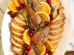 Whole dry brined roast turkey on a wooden carving board, golden brown shatteringly crisp skin glistening, garnished with fresh rosemary and thyme, dramatic side lighting