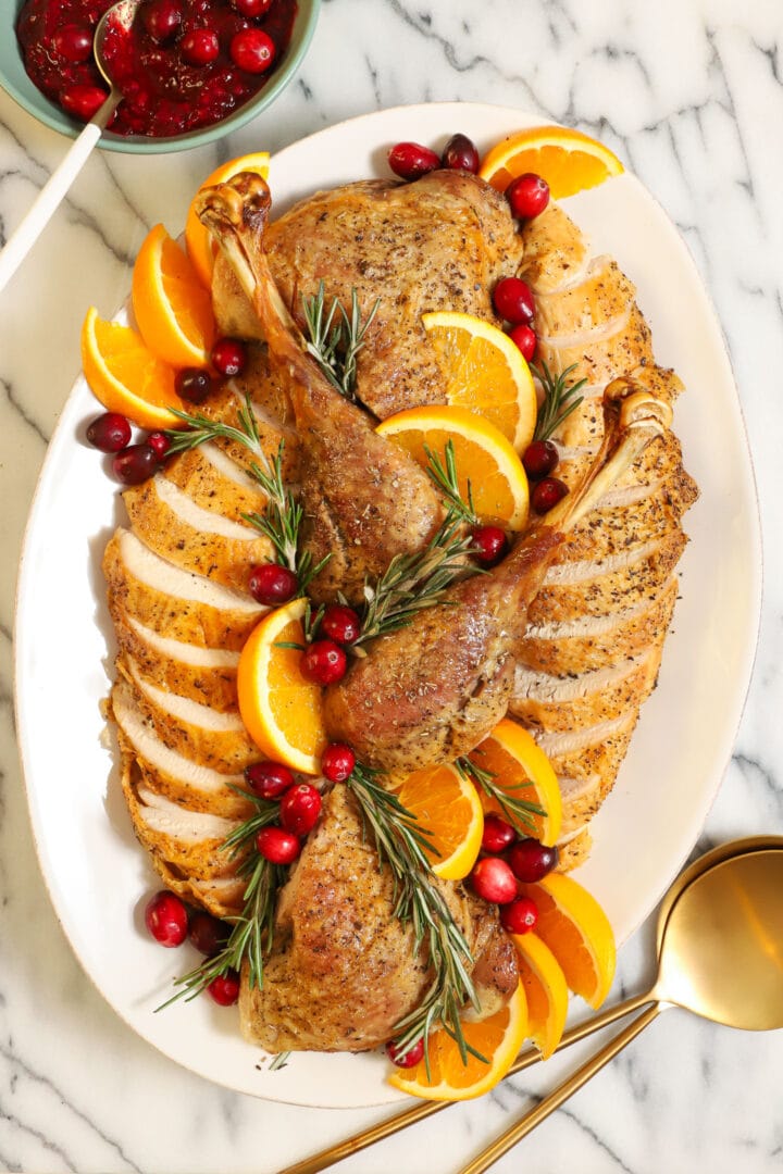Whole dry brined roast turkey on a wooden carving board, golden brown shatteringly crisp skin glistening, garnished with fresh rosemary and thyme, dramatic side lighting
