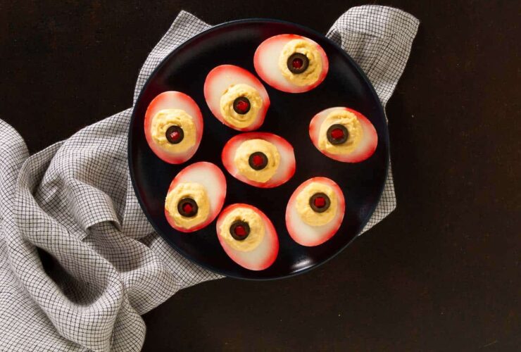 platter of eyeball deviled eggs with bloodshot hot sauce veins and olive pupils on a dark Halloween table